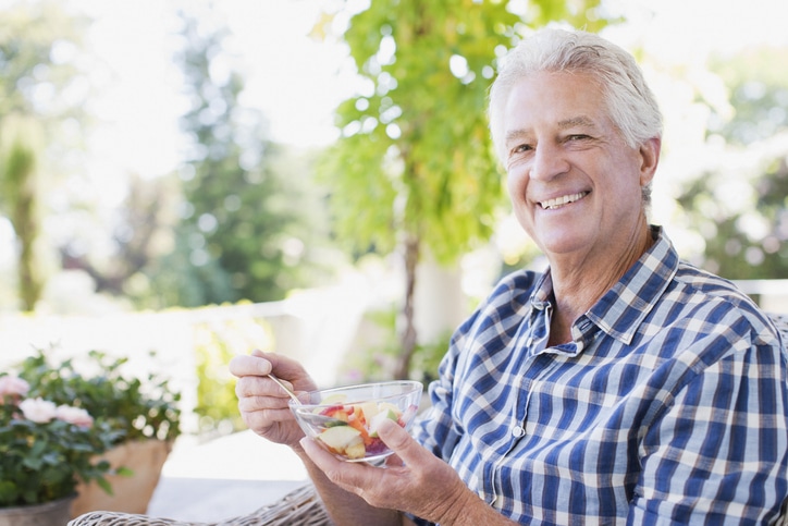 A man follows nutrition tips for managing chronic illness by eating a bowl of fresh fruit.