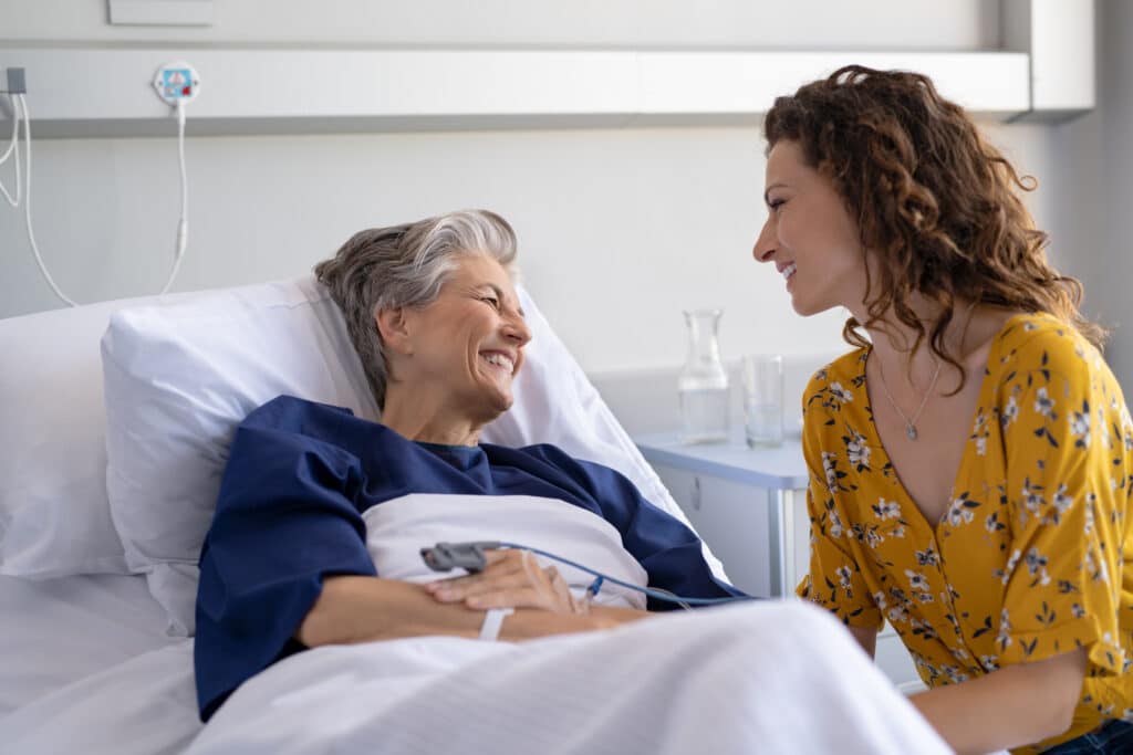 A caregiver providing Oro Valley area hospital sitter services checks on a senior laying in a hospital bed.