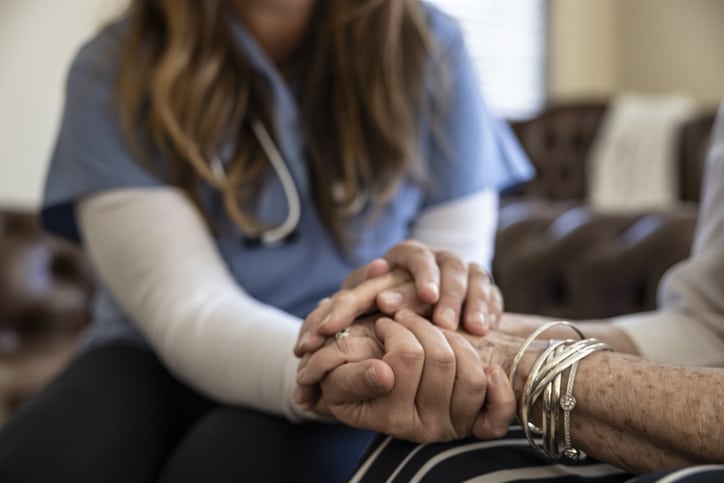 A caregiver providing hospice care in Tucson holds the hand of her elderly patient.