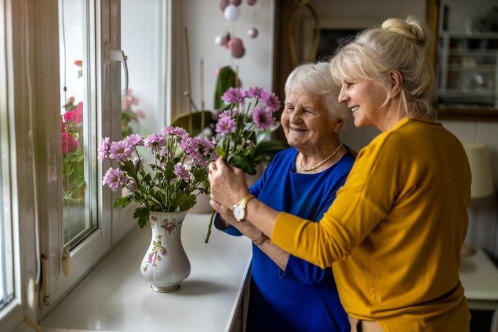 A woman who has started a new career in caregiving helps her elderly client arrange flowers.