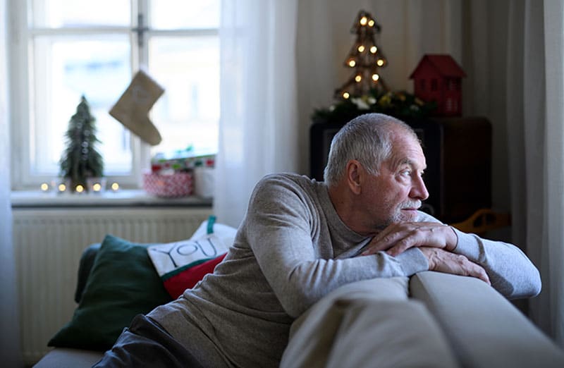 An older man experiencing post-holiday blues looks sadly out the window.