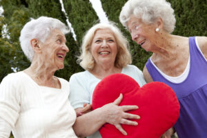 Three smiling older women hold a plush heart, symbolizing heart health for older adults.