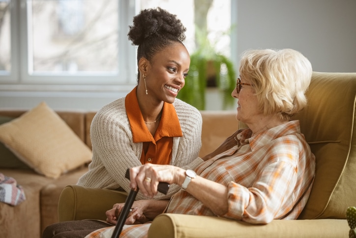 A caregiver who knows how to ease aggression and agitation in a loved one with Alzheimer’s smiles and places a calming hand on an older woman’s shoulder.