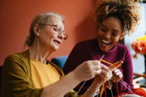 A woman who is managing tremors in Parkinson’s shows her caregiver how to knit.