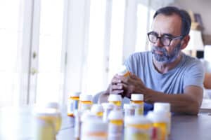 A man reviews a bunch of prescription bottles as he considers the benefits of deprescribing.