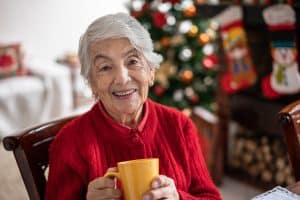 A woman celebrating the holidays with dementia smiles as she holds a cup of cocoa.