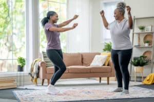 A caregiver focused on winter wellness for older adults dances with her client.