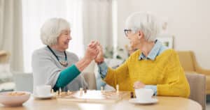 A retired woman who explores senior caregiving careers enjoys a game of chess with the person in her care.