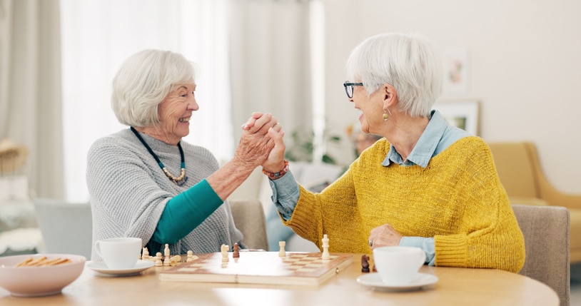 A retired woman who explores senior caregiving careers enjoys a game of chess with the person in her care.