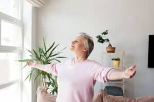 A woman with outstretched arms enjoys her bright, sunlit living room after implementing spring refresh ideas for seniors.