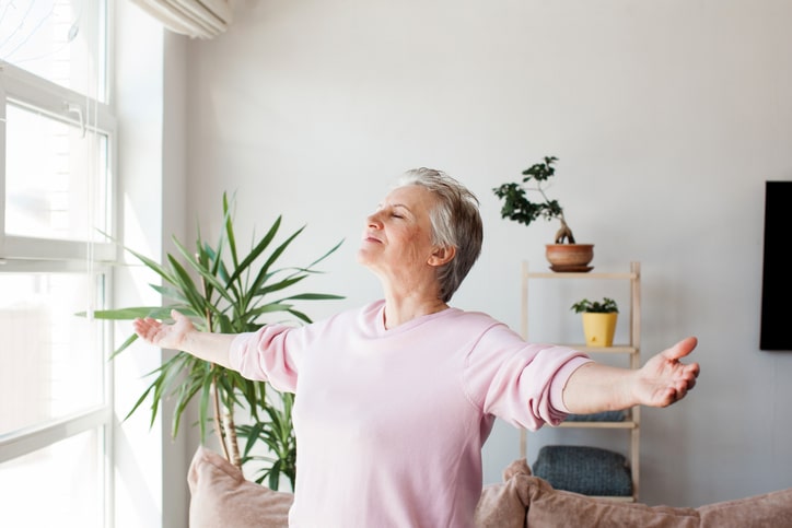 A woman with outstretched arms enjoys her bright, sunlit living room after implementing spring refresh ideas for seniors.
