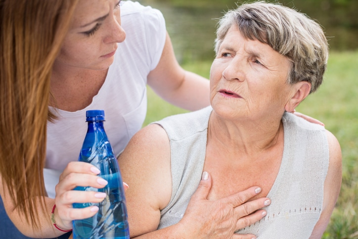 A woman hands a bottle of water to her mom, who seems to be struggling with summer fatigue in older adults.