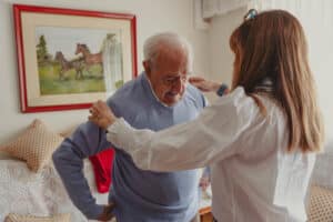 A caregiver helps an older man experiencing dressing challenges in older adults.