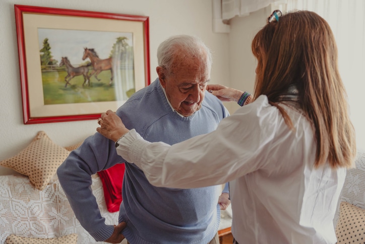 A caregiver helps an older man experiencing dressing challenges in older adults.