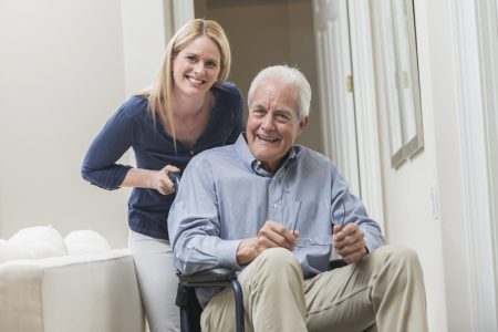 senior man sitting in a wheelchair at home with a caregiver